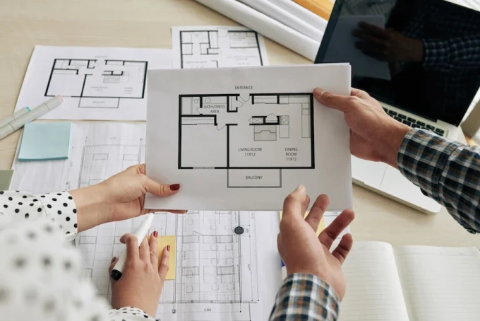 Jeune couple discutant d’un plan de logement neuf autour d’une table, avec des documents de construction