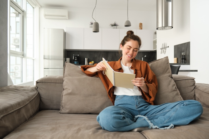 Jeune femme souriante assise dans un appartement neuf climatisé, profitant du confort intérieur pendant une journée chaude